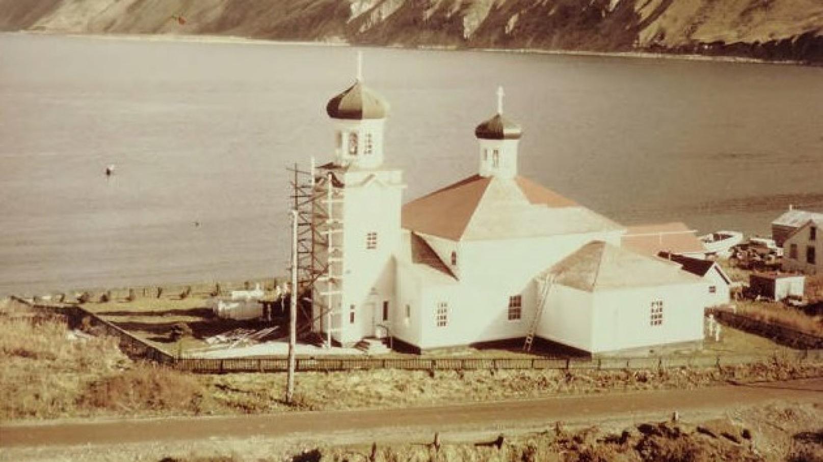 a church beside a coastal mountain is renovated with a scaffold structure on its steeple.