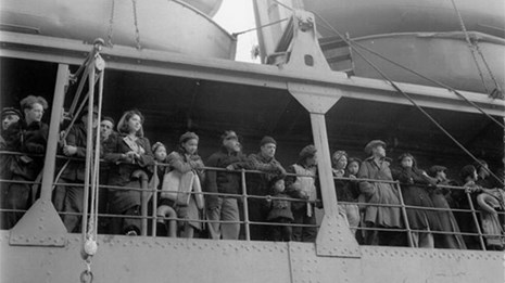 Black and white photo of people standing at boat railing.