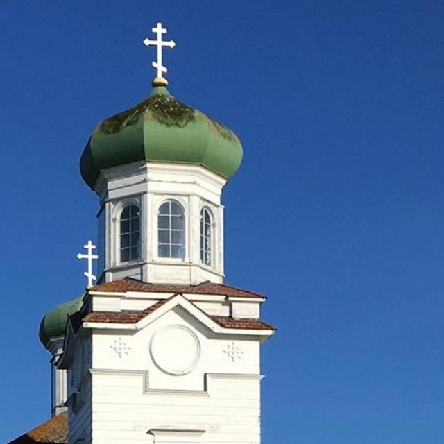 a white church with a bulbous green steeple topped with a cross.