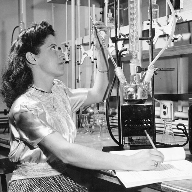 a woman looks at a glass object at a laboratory desk