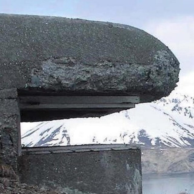 A concrete structure overlooks the ocean with snowy mountains in the background.
