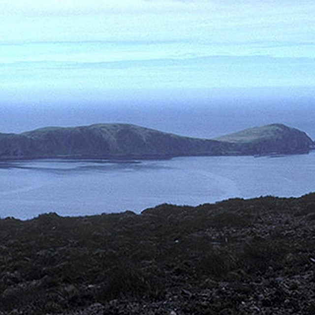 a long, low-lying island sits off the coast of a nearer, larger island.