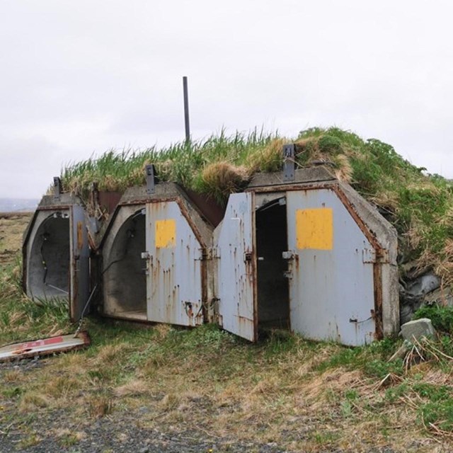 three doors open to bunker embedded in a grassy hillside.