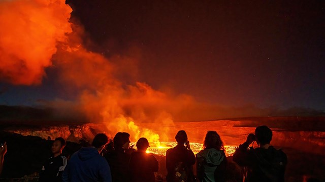 Crowd of visitors viewing a volcanic eruption from a distance, at night