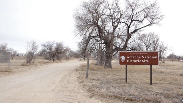 A brown sign reads "Amache National Historic Site" next to a gravel road.