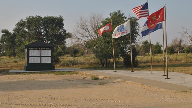 A dirt parking area with five flag poles and a small kiosk.