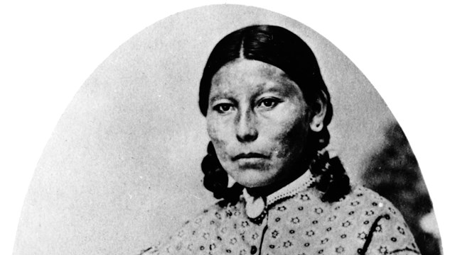 A historic photo of an indigenous woman in a high neck, long sleeved dress.