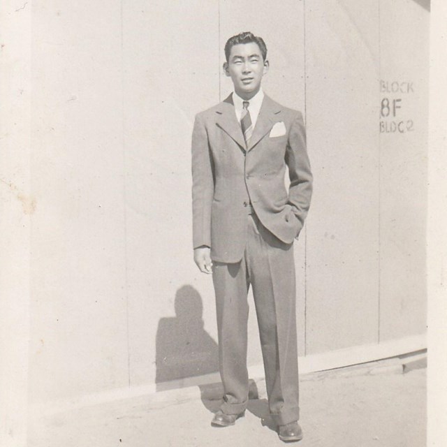 A man in a suit standing in front of a building labeled 