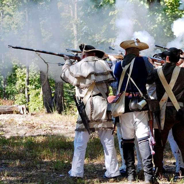 A line of Revolutionary War militiamen fire a musket volley 