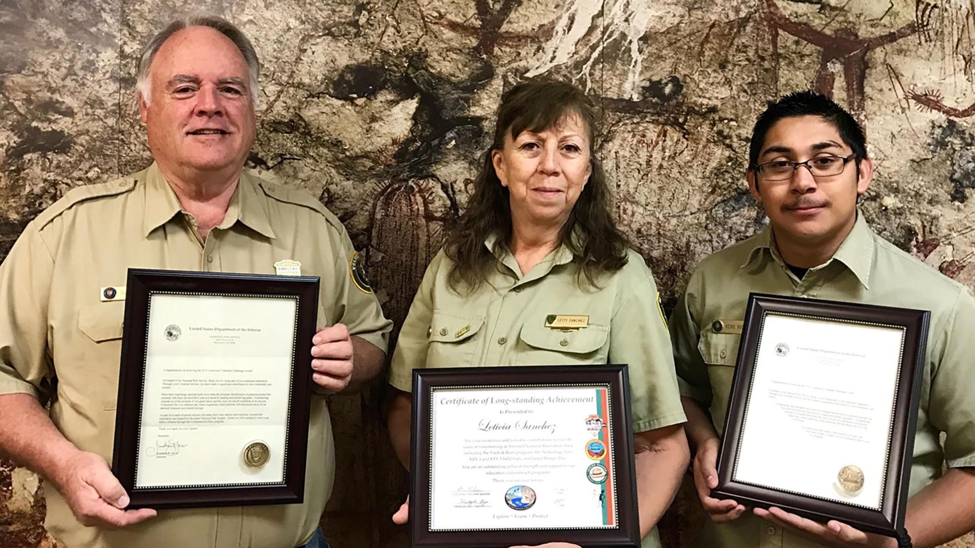 Three volunteers--an older man, a youth, and a woman--holding awards.