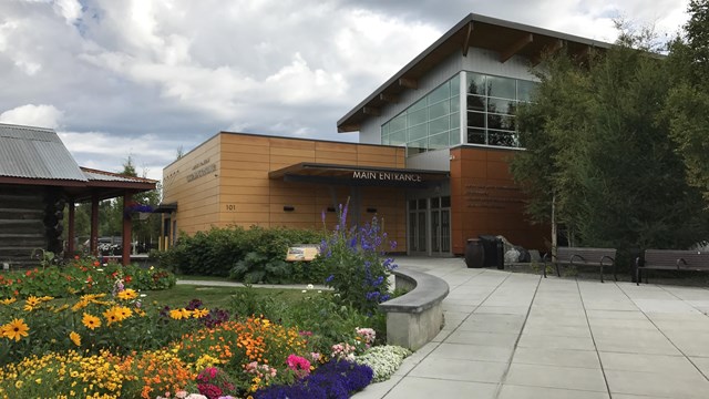 Sidewalk with flowerbeds on left side leading to large wooden building.