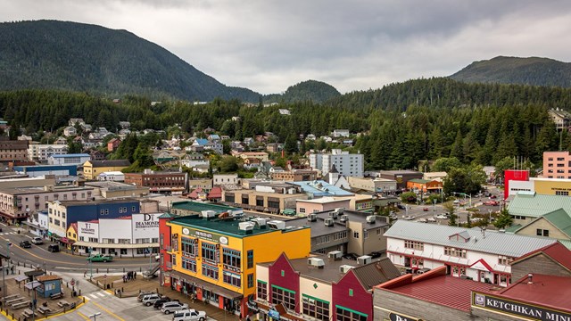 Birdseye view of small town in harbor with green mountains behind.
