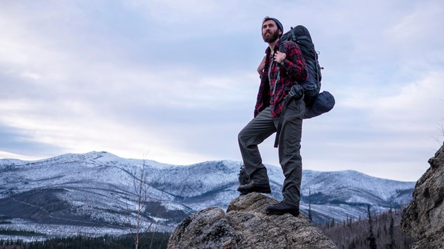 A backpacker stands atop a rocky prominence
