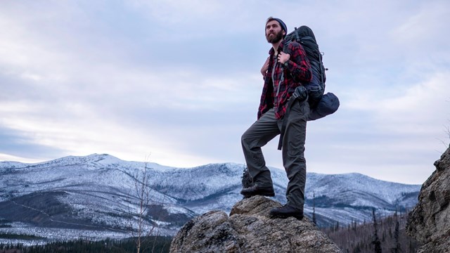 A backpacker stands atop a mountain ridge.