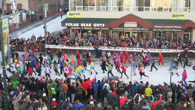 Birdseye view of city street with snow on road and large crowd gathered on edges watching runners.