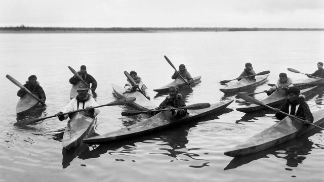 Black and white photo of people in canoes on water.