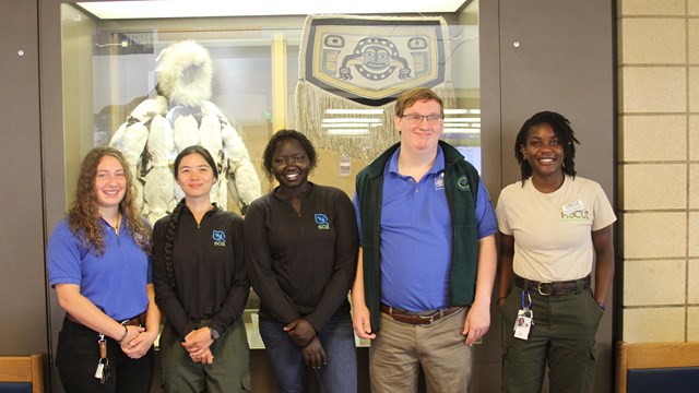 Five youths standing indoors in front of an exhibit in formal pose.