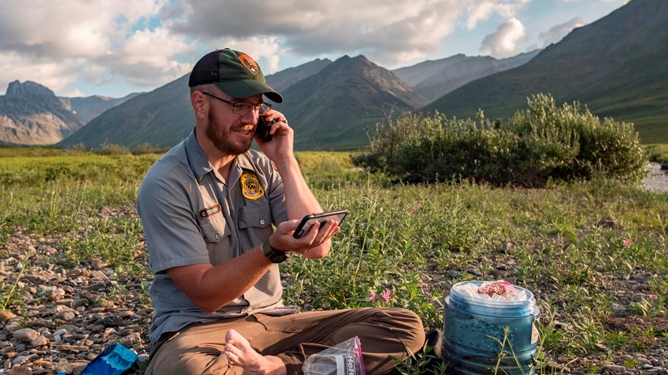 A park ranger talks on a satellite phone in a mountain valley