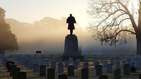 Fog rests on hundreds of graves and a stone monument of a Civil War soldier