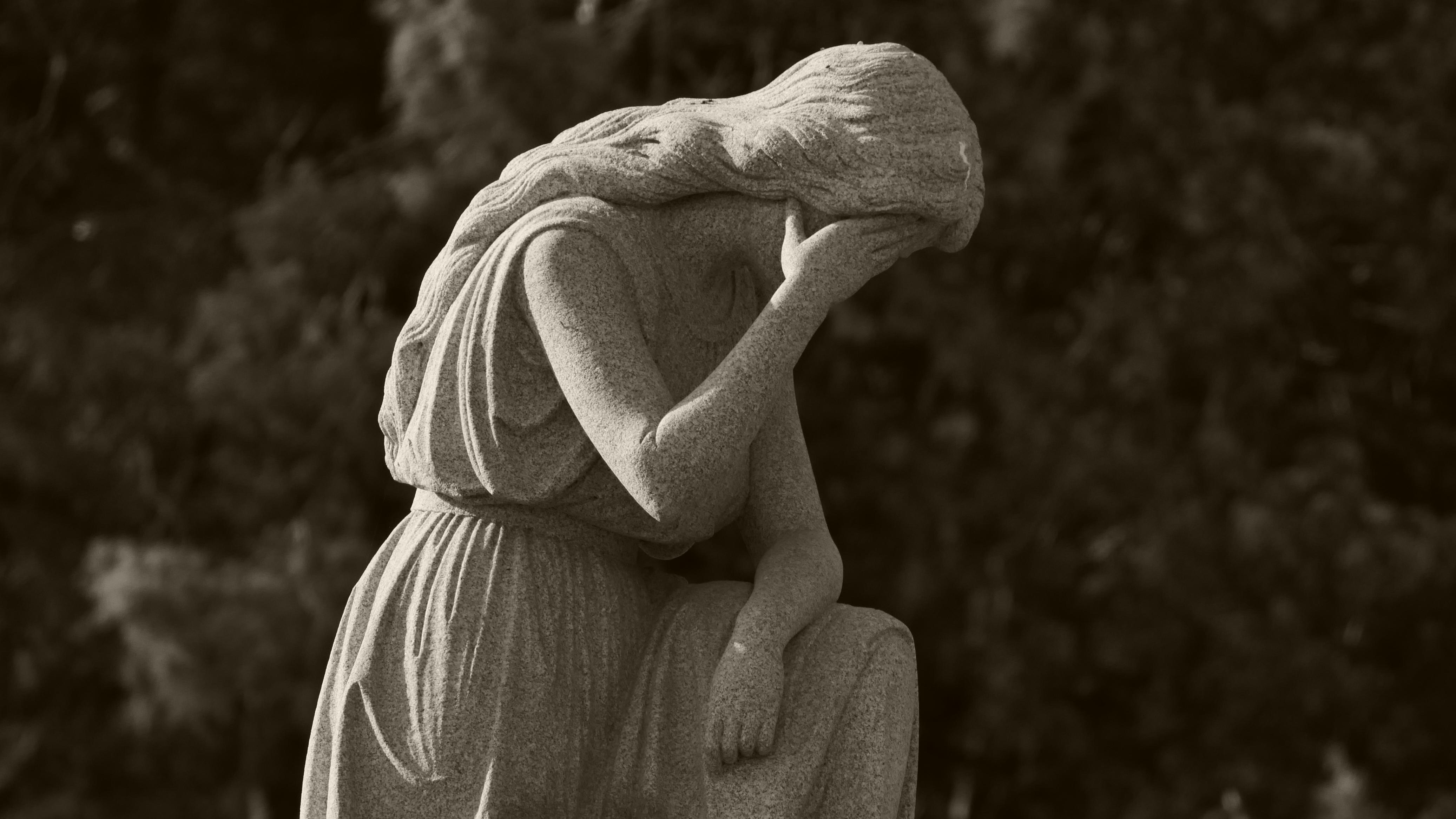 A stone woman kneeling with her face lowered in one hand.
