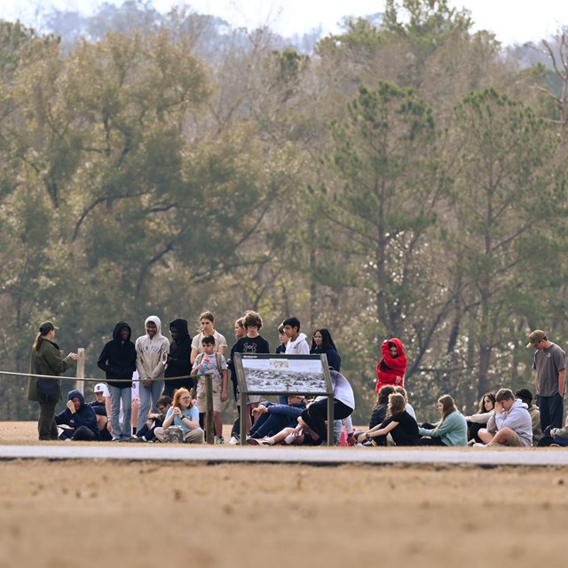 A ranger in green and gray uniform giving students a tour in prison site.