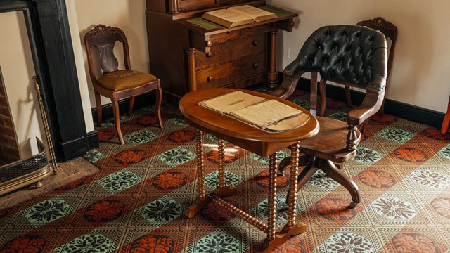 A wheeled leather chair in front of a wooden table with documents spread out on top.