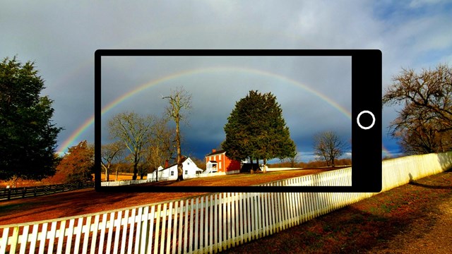 Black smartphone frame around the two story brick McLean House with deep blue clouds and a rainbow.