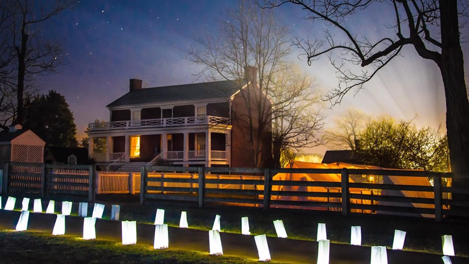 Brick McLean House backlit by the glow of a setting sun and luminary candles in front