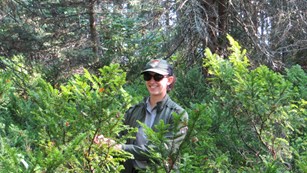 Female ranger standing in tall green bushes in wooden area.