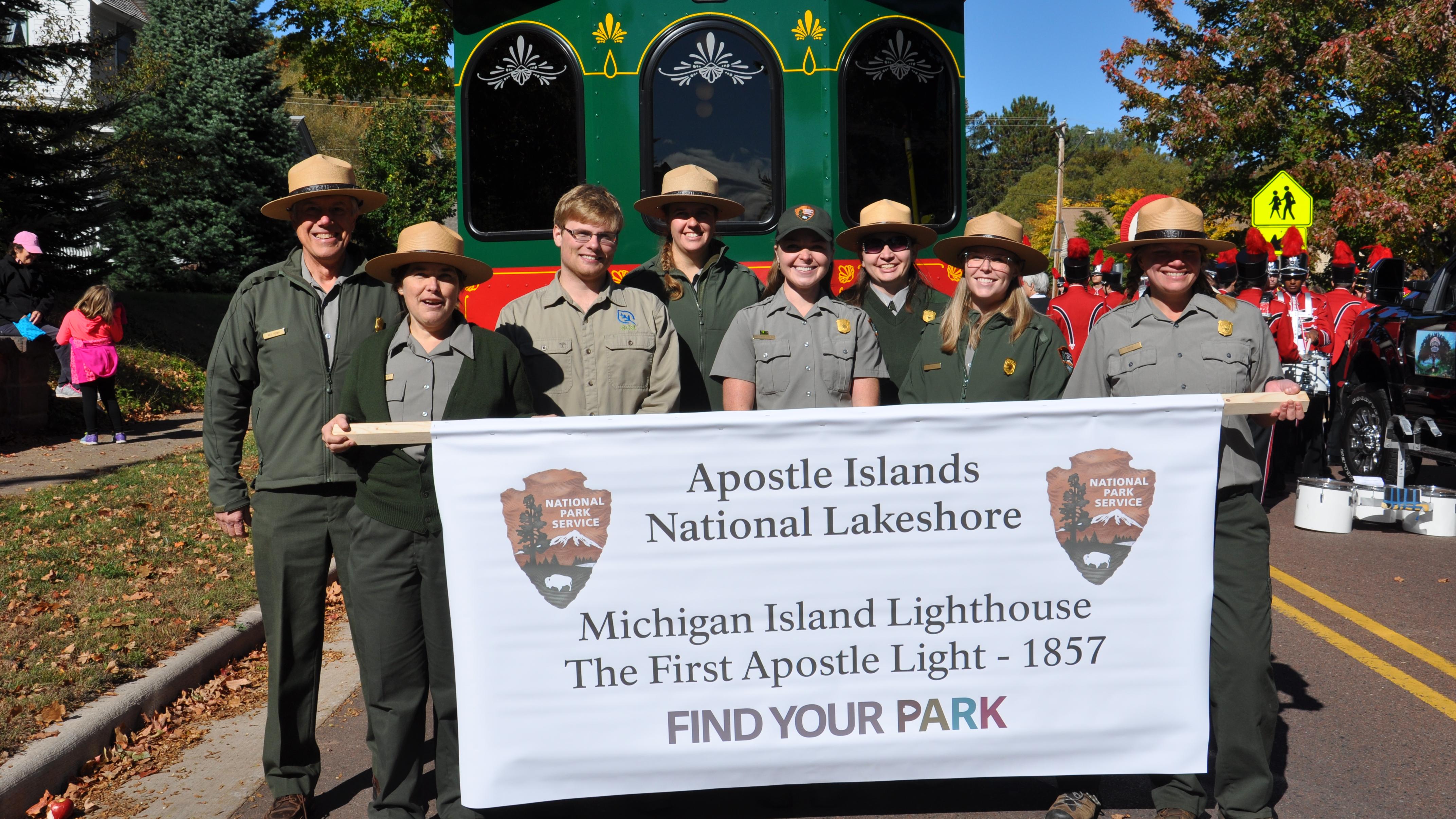 8 people standing holding park banner in front of trolley.