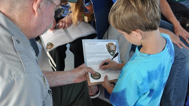 Young child signing a certificate with a park ranger.