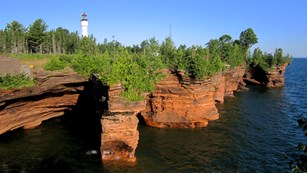Sandstone cliffs on lake with white lighthouse tower in background.