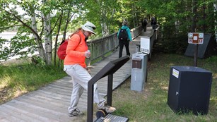 A hiker scrapes their boot on a brush to clean off dirt and debris.