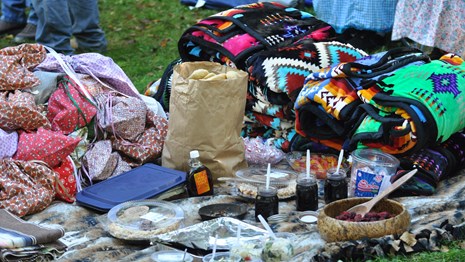 A blanket on the ground, covered with cloth bundles, food, and colorful folded blankets.