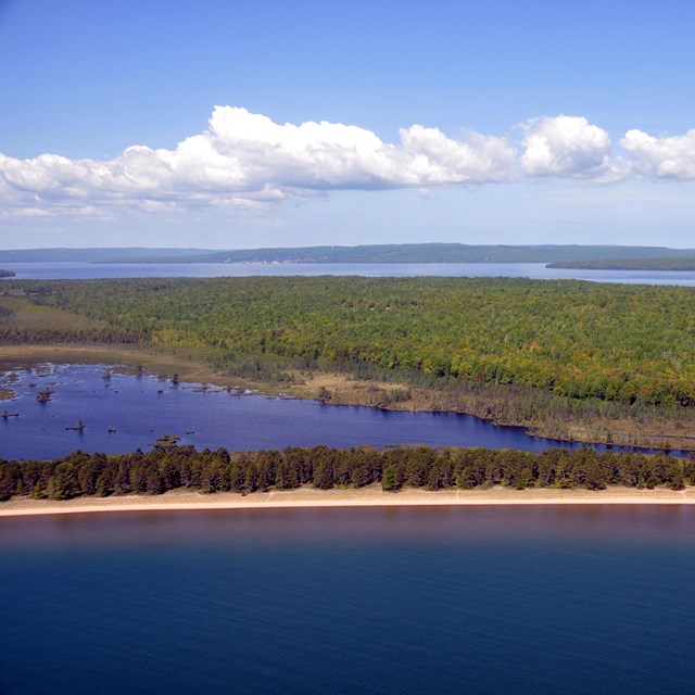An aerial view of a beach, woods, and lagoon along the lake. 