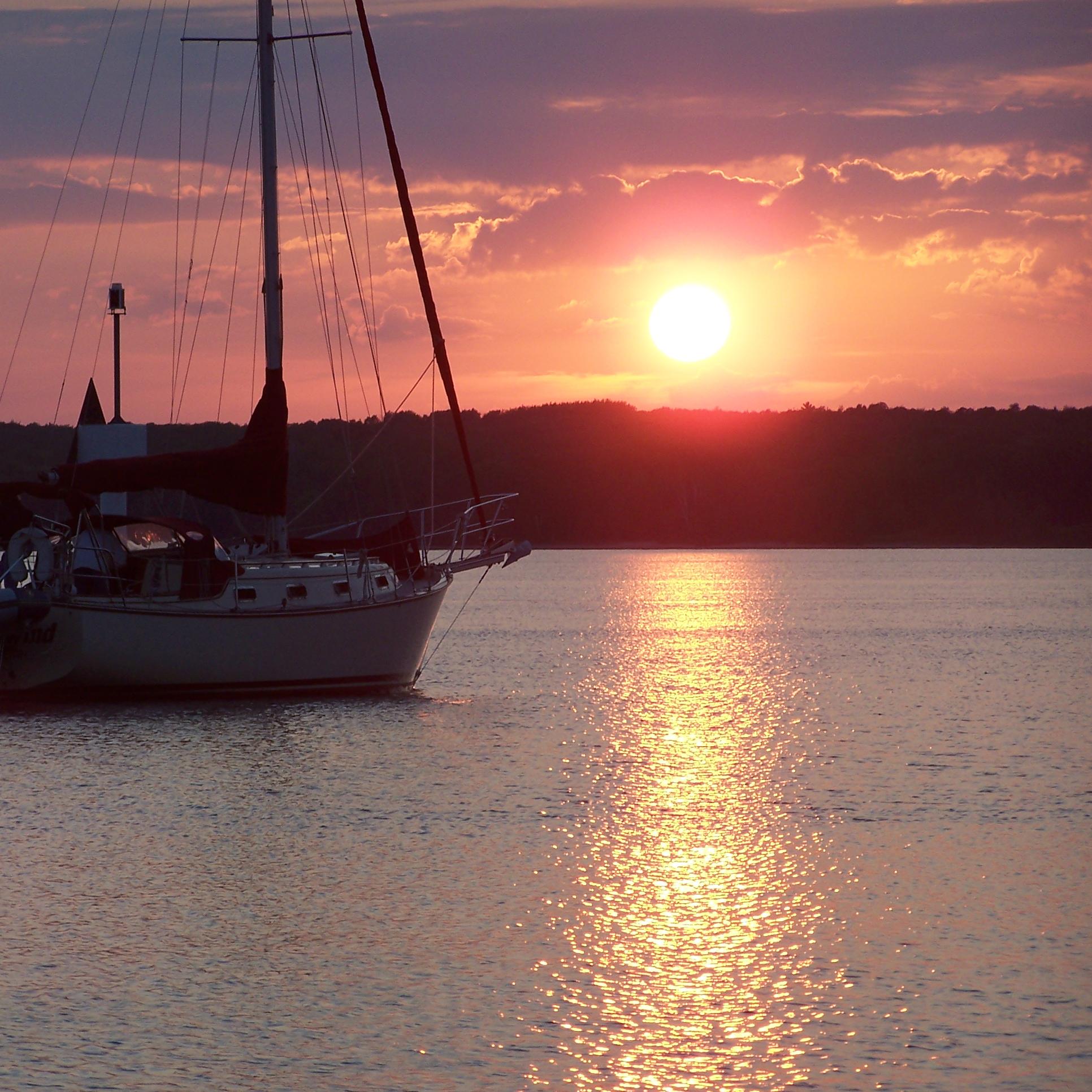 Sunset across the lake behind a dark island with a moored boat on the left.