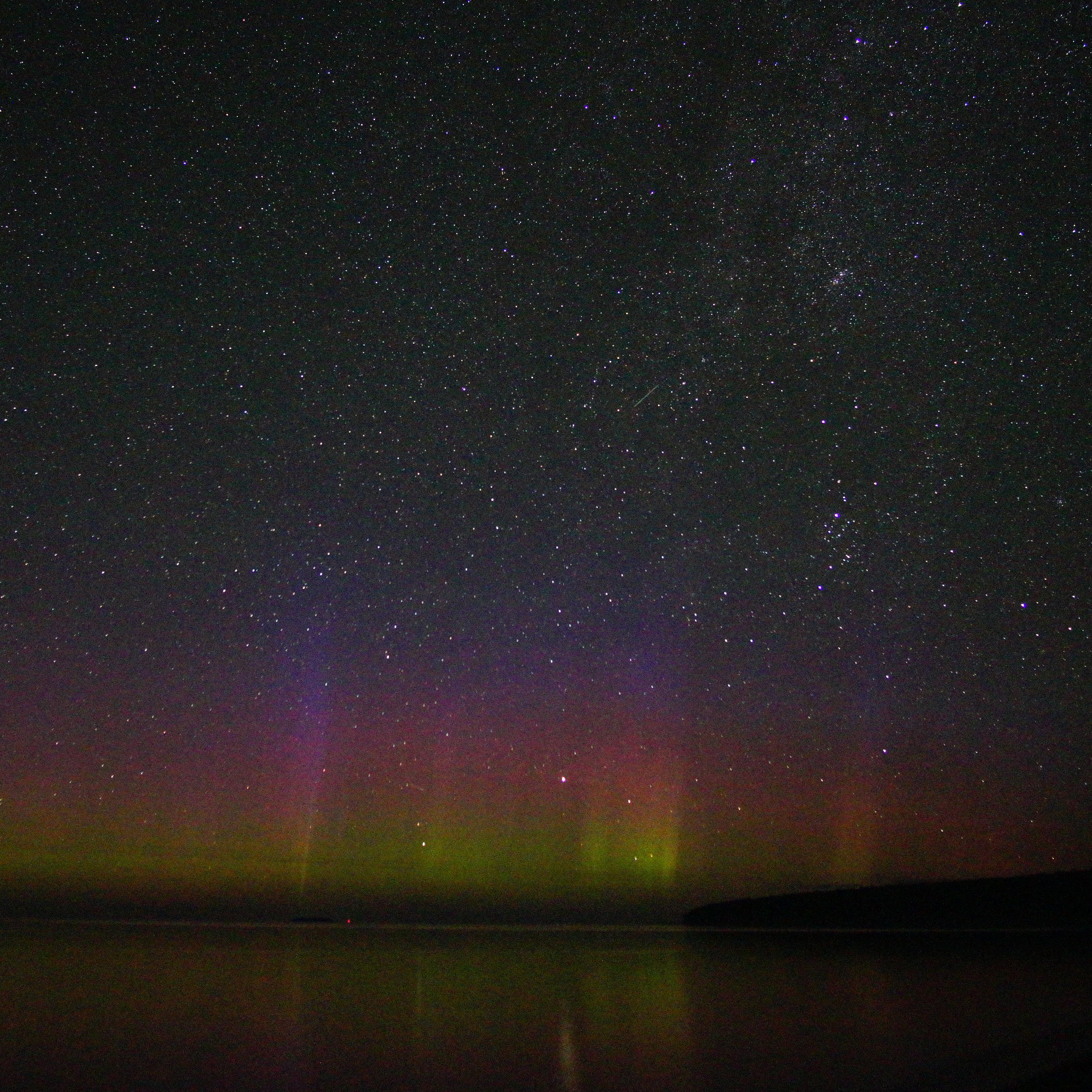 Northern lights in the night sky above land silhouette.