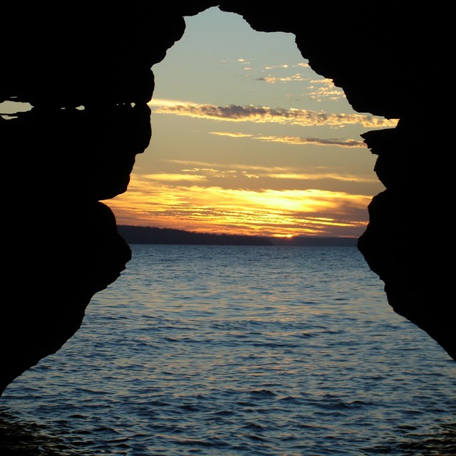 A orange and yellow sunset over lake Superior viewed through a sea cave archway