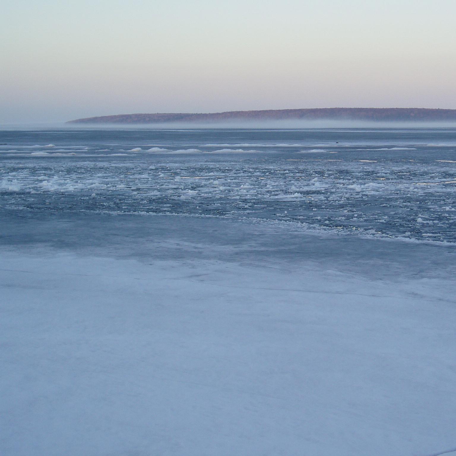 Winter light sky with a partially frozen lake and purple island in the distance.