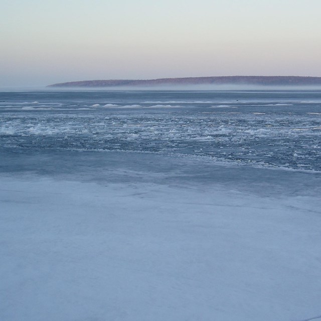 Winter light sky with a partially frozen lake and purple island in the distance.