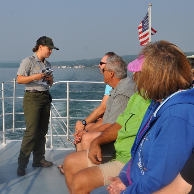 NPS park ranger distributing brochures to people on the upper tier of a cruise ship.