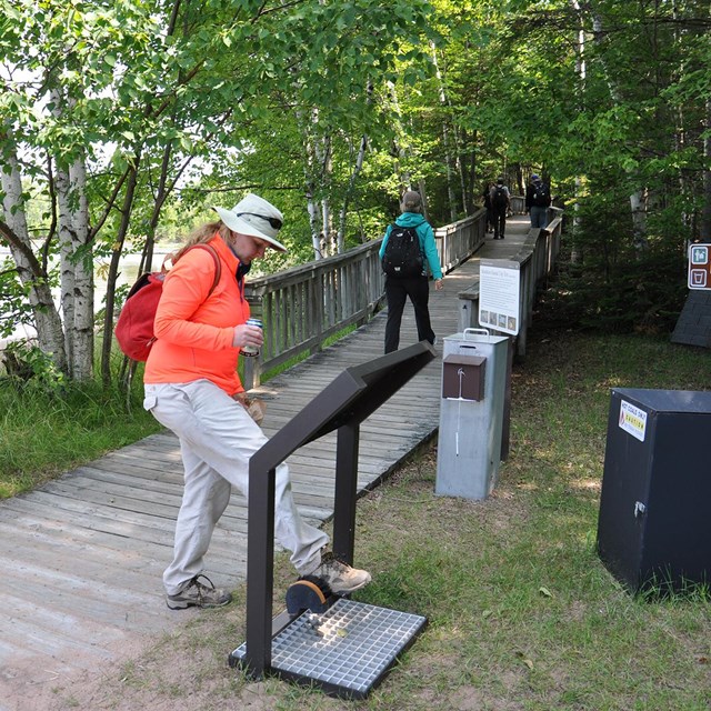 A hiker scrapes their boot on a brush to clean off dirt and debris. 