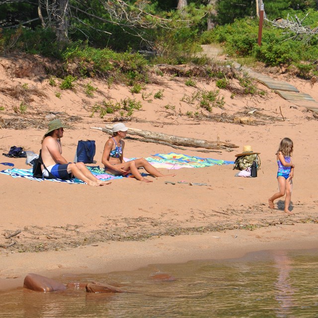 Family of 3 sitting on a sandy beach.