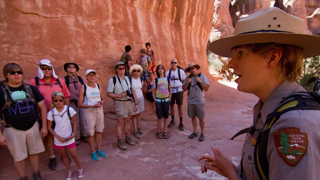 a ranger speaks to a group of people in front of a rock wall