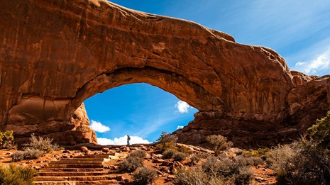 a distant person is dwarfed by a massive rock arch