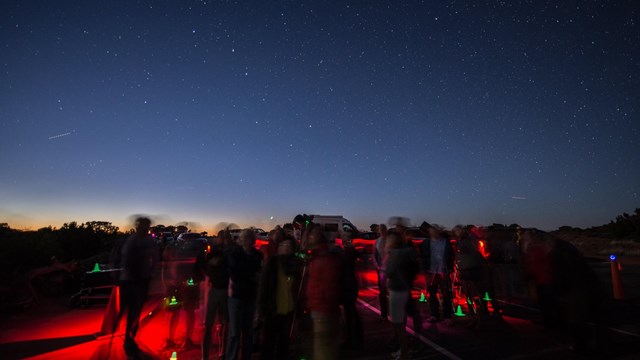 A group of people surrounded by red and green lights stand in the dark under a starry sky