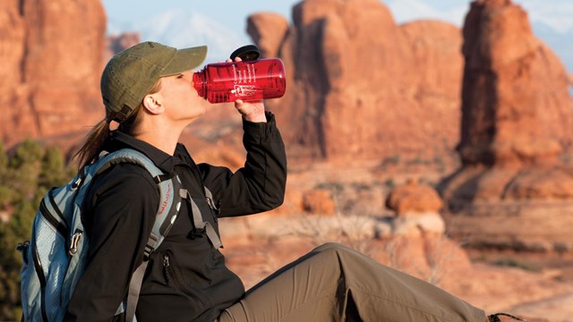 a woman drinks water from a red bottle