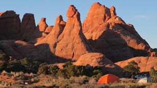 an orange tent sits beneath high red rock walls