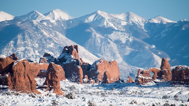 snow-dusted redrock arch, pinnacles, with mountains in the background