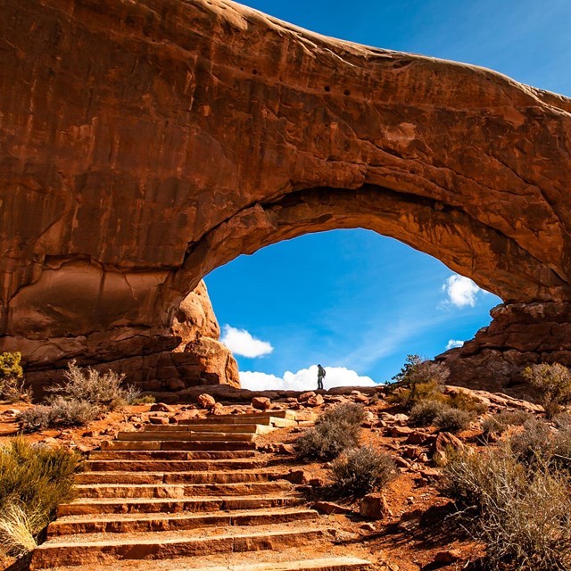 a distant person is dwarfed by a massive rock arch